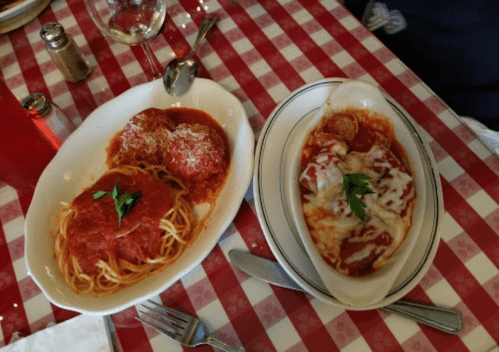 Two plates of Italian food: spaghetti with meatballs in marinara sauce and baked pasta with cheese, both garnished with parsley.