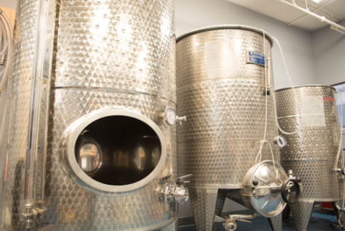 Three large, shiny stainless steel fermentation tanks in a winery setting.