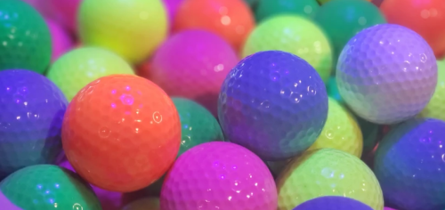 A close-up of colorful golf balls in vibrant shades of pink, green, orange, and purple, creating a playful, lively scene.