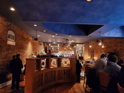 Interior of a restaurant with brick walls, blue ceiling, and warm lighting, featuring a bar and dining area.