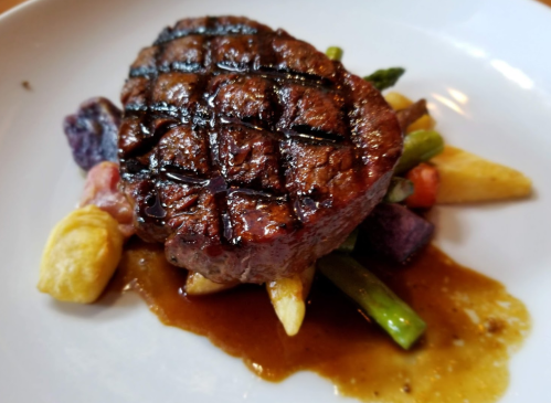 A perfectly grilled steak on a bed of colorful vegetables, drizzled with savory sauce.