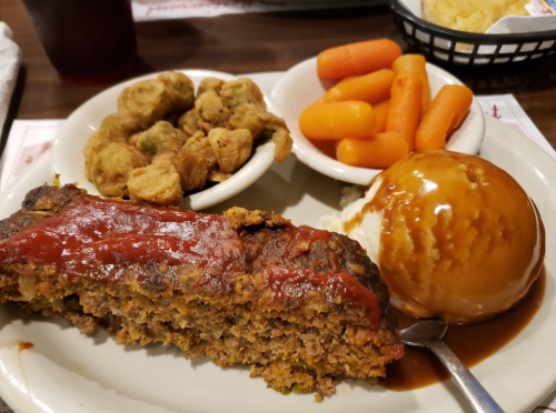 A plate featuring meatloaf with ketchup, mashed potatoes, okra, and carrots, alongside a scoop of ice cream.