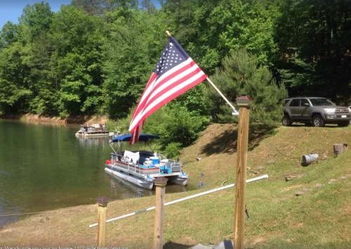 A U.S. flag waves near a lake with boats and greenery in the background.