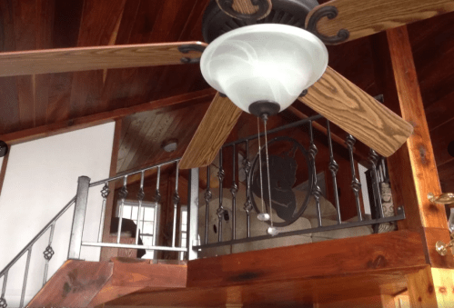 A wooden ceiling fan hangs above a staircase with a decorative railing and a wall featuring a circular design.