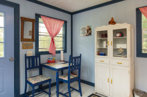 Cozy room with blue walls, a small table and chairs, a white cabinet, and bright curtains.