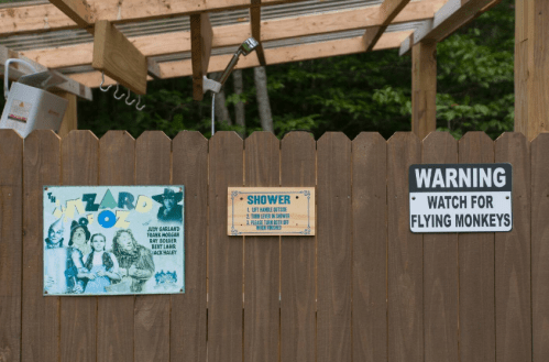 A wooden fence with signs: one for a shower, a whimsical "Wizard of Oz" poster, and a warning for flying monkeys.