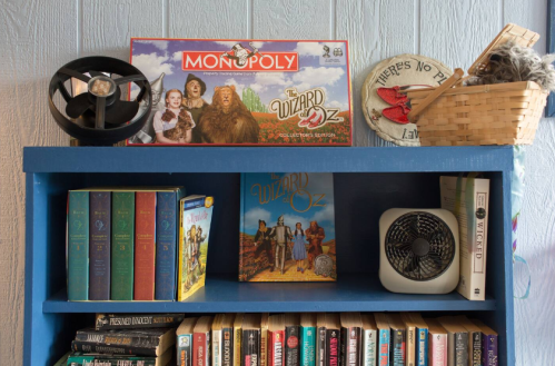 A blue bookshelf displaying "The Wizard of Oz" book, Monopoly game, and various vintage items and books.