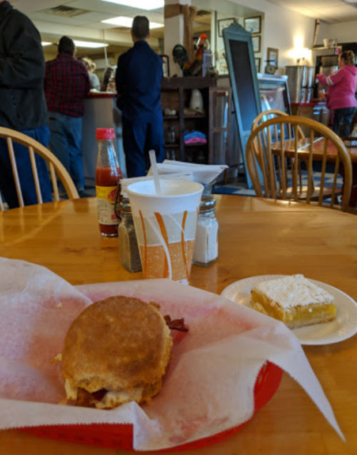 A table with a sandwich, dessert, and condiments, with people in the background at a casual dining restaurant.