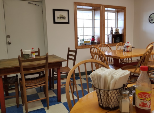 Cozy dining area with wooden tables, chairs, and condiments, featuring large windows and a rustic decor.