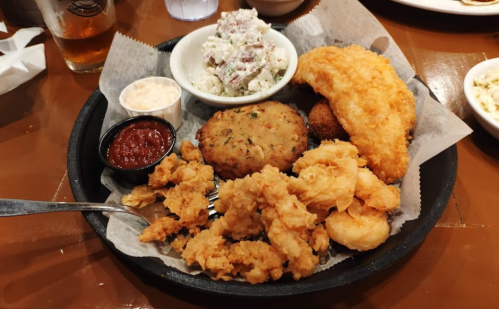 A platter of fried seafood, hushpuppies, coleslaw, and dipping sauce served in a basket.