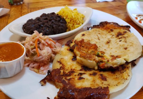 A plate of pupusas with beans, yellow rice, pickled vegetables, and a side of sauce.