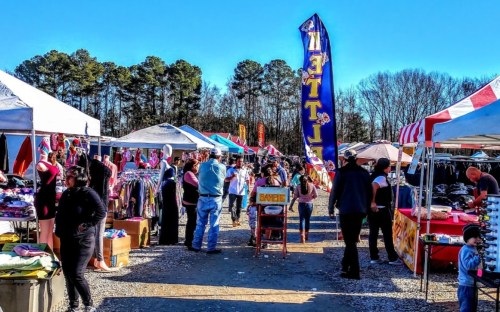 A bustling outdoor market with colorful tents, shoppers browsing, and a large "Sale" sign in the foreground.