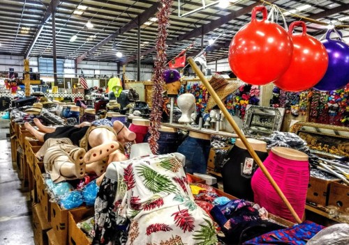 A bustling market scene filled with colorful clothing, mannequins, and large inflatable balls.
