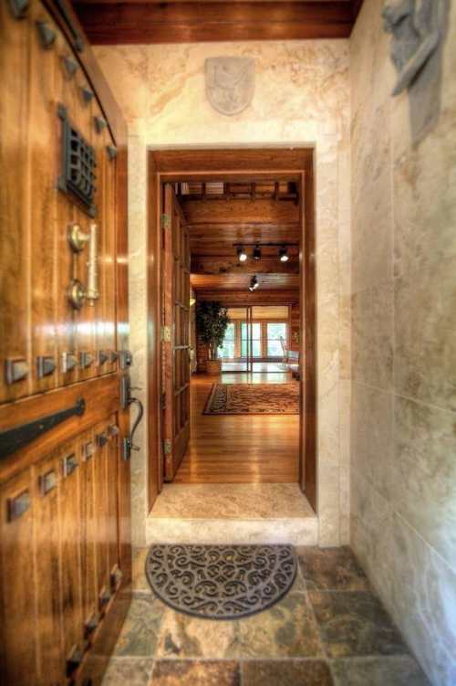 A wooden front door opens to a spacious, warmly lit interior with stone flooring and a view of a cozy living area.