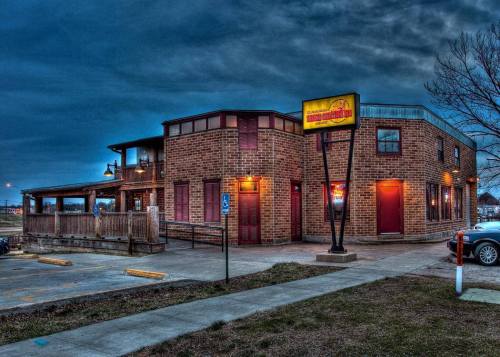 A brick building with a sign, illuminated at dusk, featuring a patio and parking area.