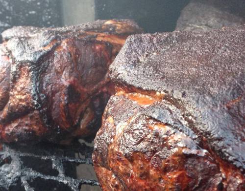 Close-up of smoked meat on a grill, showcasing a dark, charred exterior with juicy textures.