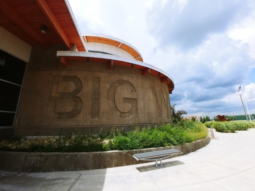 Exterior view of a building featuring a large "BIG W" inscription on a textured wall, with a cloudy sky above.