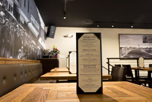 A restaurant menu stands on a wooden table, with a vintage black-and-white photo in the background.