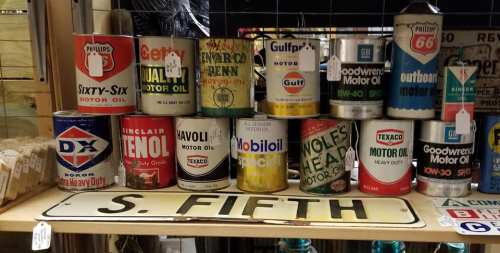 A collection of vintage motor oil cans displayed on a shelf, with a sign reading "S. FIFTH" underneath.