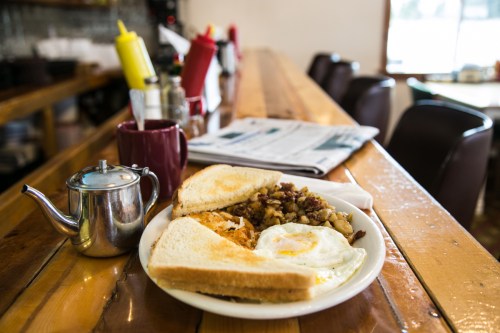 A plate of breakfast with eggs, toast, and hash browns on a wooden table, with a coffee mug and condiments in the background.