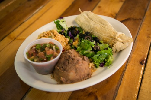 A plate of Mexican food featuring tamale, refried beans, rice, salad, and salsa on a wooden table.