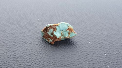 A rough turquoise stone with brown matrix, resting on a textured black surface.