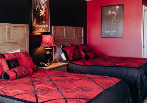 A cozy hotel room with two beds, red and black decor, and Twilight movie posters on the walls.