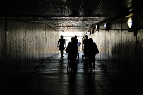 Silhouettes of people walking through a dimly lit tunnel, with light at the end illuminating the scene.