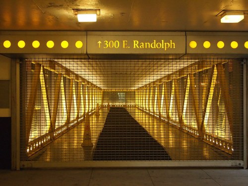 A well-lit, gated walkway with yellow lights and a sign for 300 E. Randolph, featuring a modern architectural design.