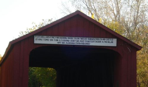 Sign on a red covered bridge warns of a $5 fine for driving more than 12 horses or cattle or for leading them too fast.
