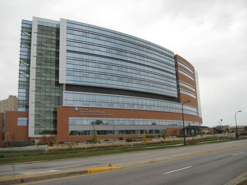 Modern hospital building with large glass windows and brick facade, set against a cloudy sky.
