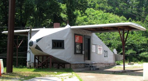 A unique building designed to resemble an airplane, set in a green, wooded area.