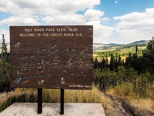 Sign at Salt River Pass, elevation 7630, welcoming visitors to Greys River Road, with a scenic mountain view in the background.