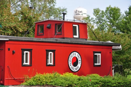 A red train caboose with a circular "Northern Pacific Railway" logo, surrounded by greenery and a water tower in the background.