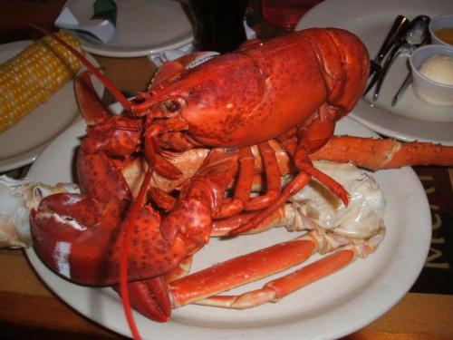 A plate featuring a large red lobster, crab legs, and corn on the cob, served in a casual dining setting.