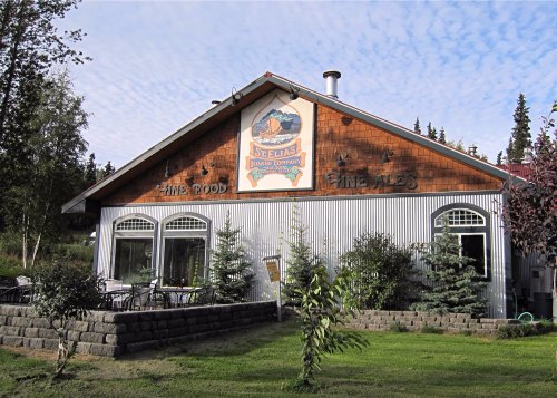 Exterior of St. Elias Brewing Company featuring a wooden facade, sign, and outdoor seating area surrounded by trees.