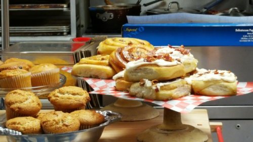 A display of freshly baked pastries, including cinnamon rolls and muffins, on a table with a checkered cloth.