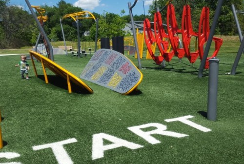 A child explores a colorful playground with climbing structures and a grassy area marked "START."