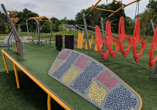 Colorful playground equipment with climbing structures and a textured surface on a grassy area.