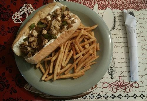 A sandwich filled with grilled chicken, peppers, and onions, served with a side of crispy French fries on a plate.