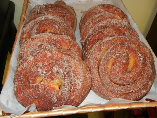 A tray of cinnamon rolls coated in sugar, arranged in a spiral shape on parchment paper.