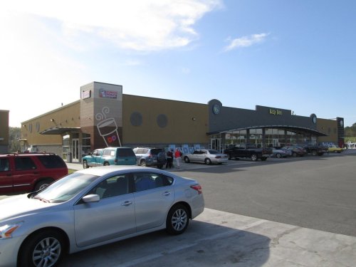 A large retail building with a coffee shop, surrounded by parked cars and a clear blue sky.