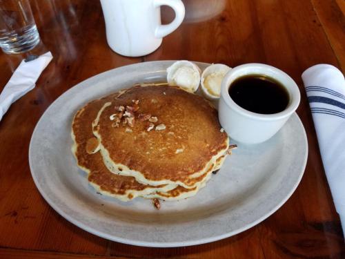 A plate of three pancakes topped with chopped nuts, served with a small cup of syrup and two dollops of butter.