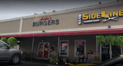 A storefront featuring "Anita's Burgers" and "Sideline Barber Shop," with outdoor seating and greenery.