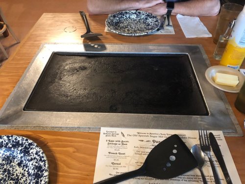 A table setting with a large griddle, plates, utensils, and a menu, ready for cooking.