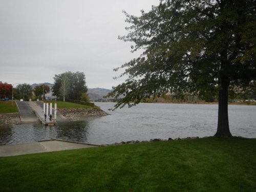 A calm river scene with a grassy shore, a tree, and a boat dock under a cloudy sky.