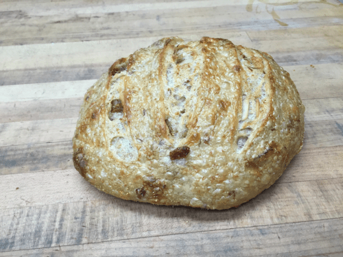 A freshly baked round loaf of bread with a golden crust and scored top, resting on a wooden surface.