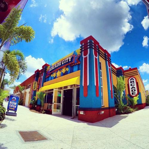 Colorful exterior of Arcade City with palm trees and a bright blue sky, featuring a "Now Open" sign.