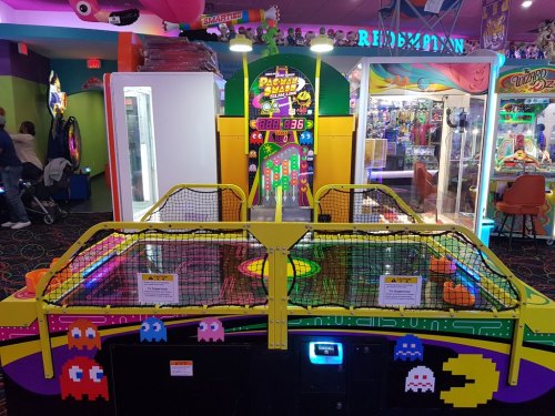 A colorful arcade with a Pac-Man game and air hockey table, surrounded by various games and bright decorations.