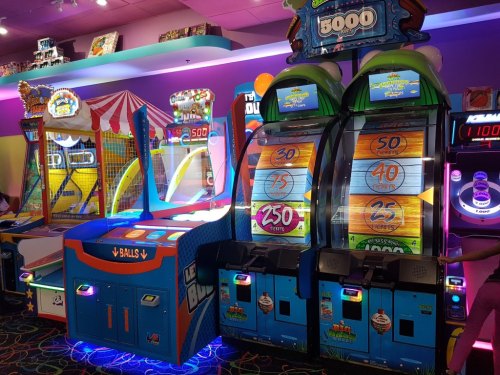 Colorful arcade games with bright lights, including a ball toss and slot machines, in a vibrant entertainment space.